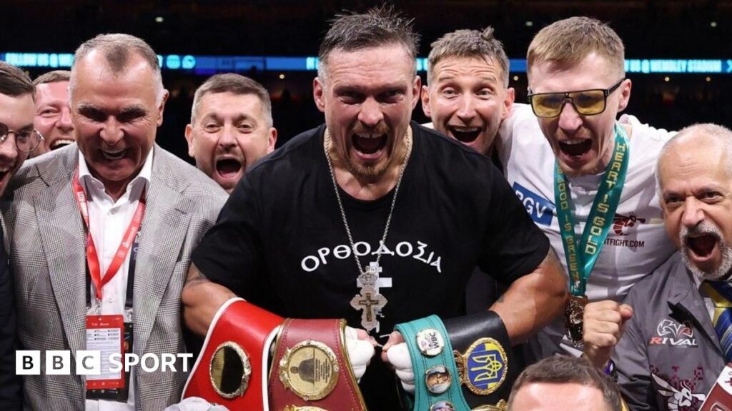 Oleksandr Usyk holds up his arms as Daniel Dubois walks past in the ring at Wembley Stadium