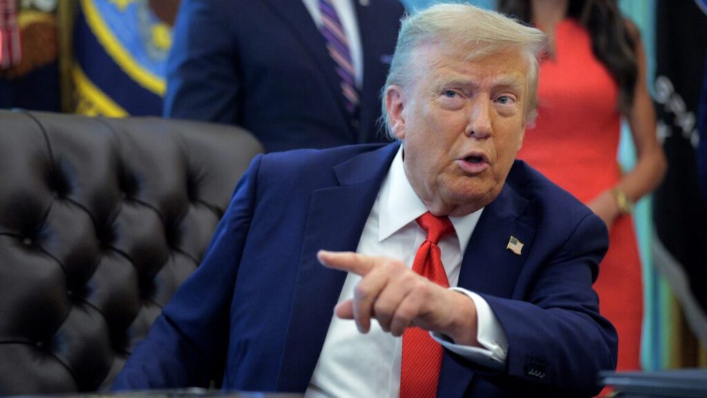 President Donald Trump sits at his desk and talks while pointing a finger.
