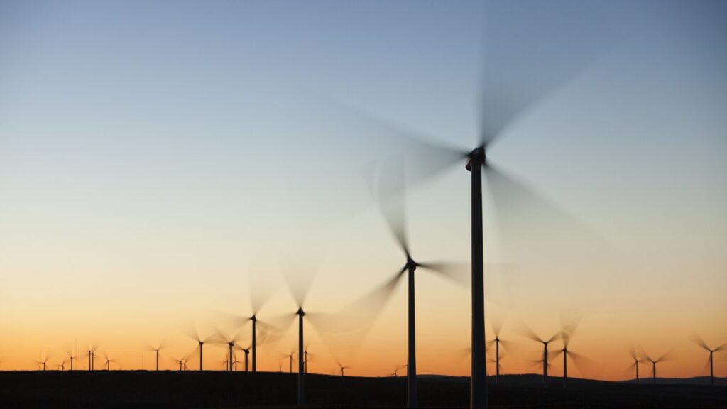 Wind turbines in front of a sunrise, with their blades blurred due to their motion.