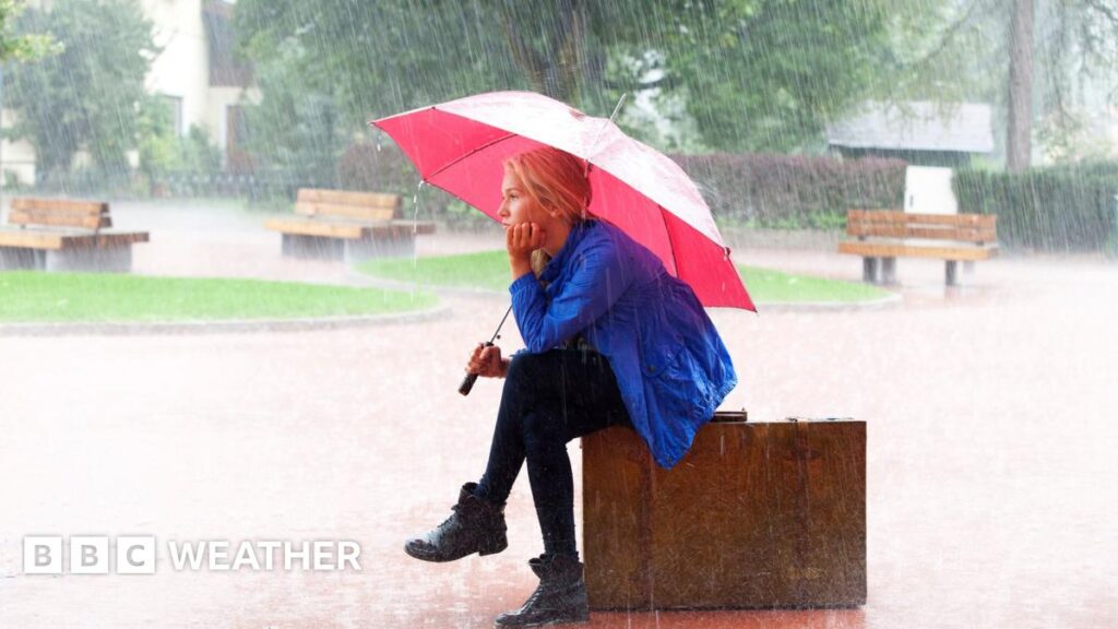 A photo of a woman beneath an umbrella sheltering from heavy rain