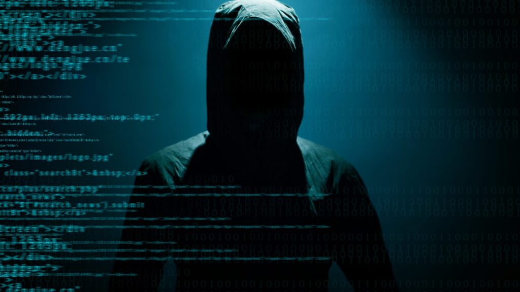 Stock photo of a hooded figure hiding behind computer code.