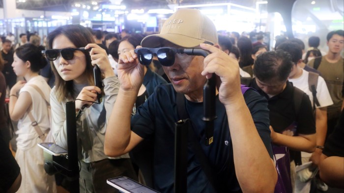 Can smart glasses ever earn our trust? Visitors try on AR+AI glasses at the XREAL booth, surrounded by a crowd at a technology expo.