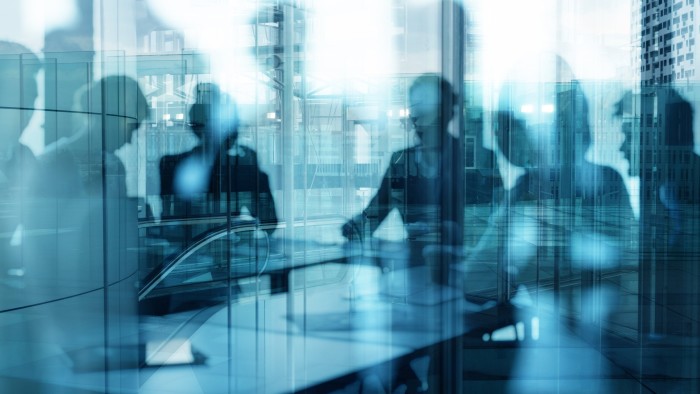 Britain’s ‘fit note’ system faces shake-up to get more people back to work Silhouetted figures of business people in an office are layered with reflections of modern glass buildings.