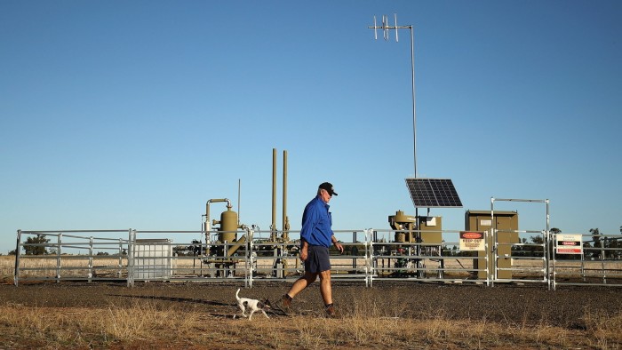 Energy dealmaker XRG revamps leadership after $40bn acquisition spree A man walks with a small dog past a Santos pilot well on his farm in Australia, with equipment and warning signs visible.