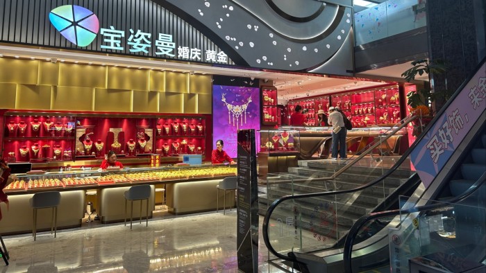 Gold rally dents sales at China’s jewellery retailers A brightly lit jewellery store with glass display cases filled with gold items and staff behind the counters.