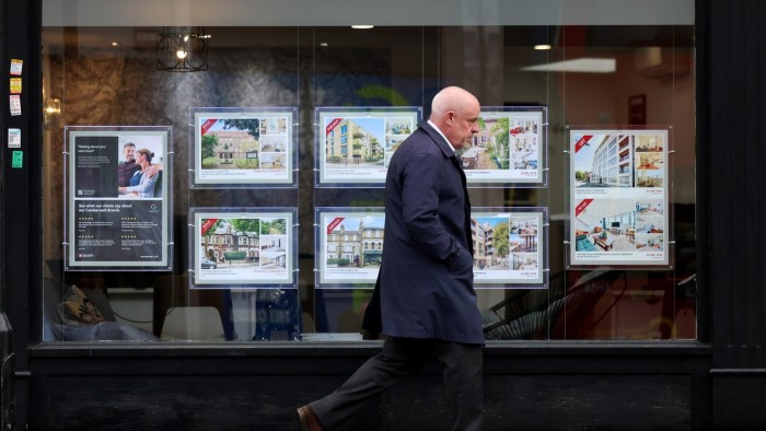 UK house prices edge higher despite Budget uncertainty A man walks past a London real estate agency window displaying property listings with "sold" and "let" signs.